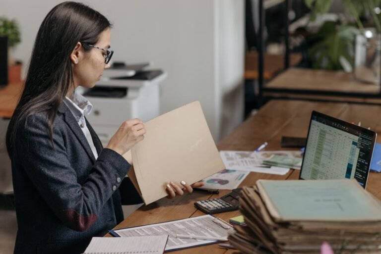Professional reviewing folders and financial records beside a laptop.